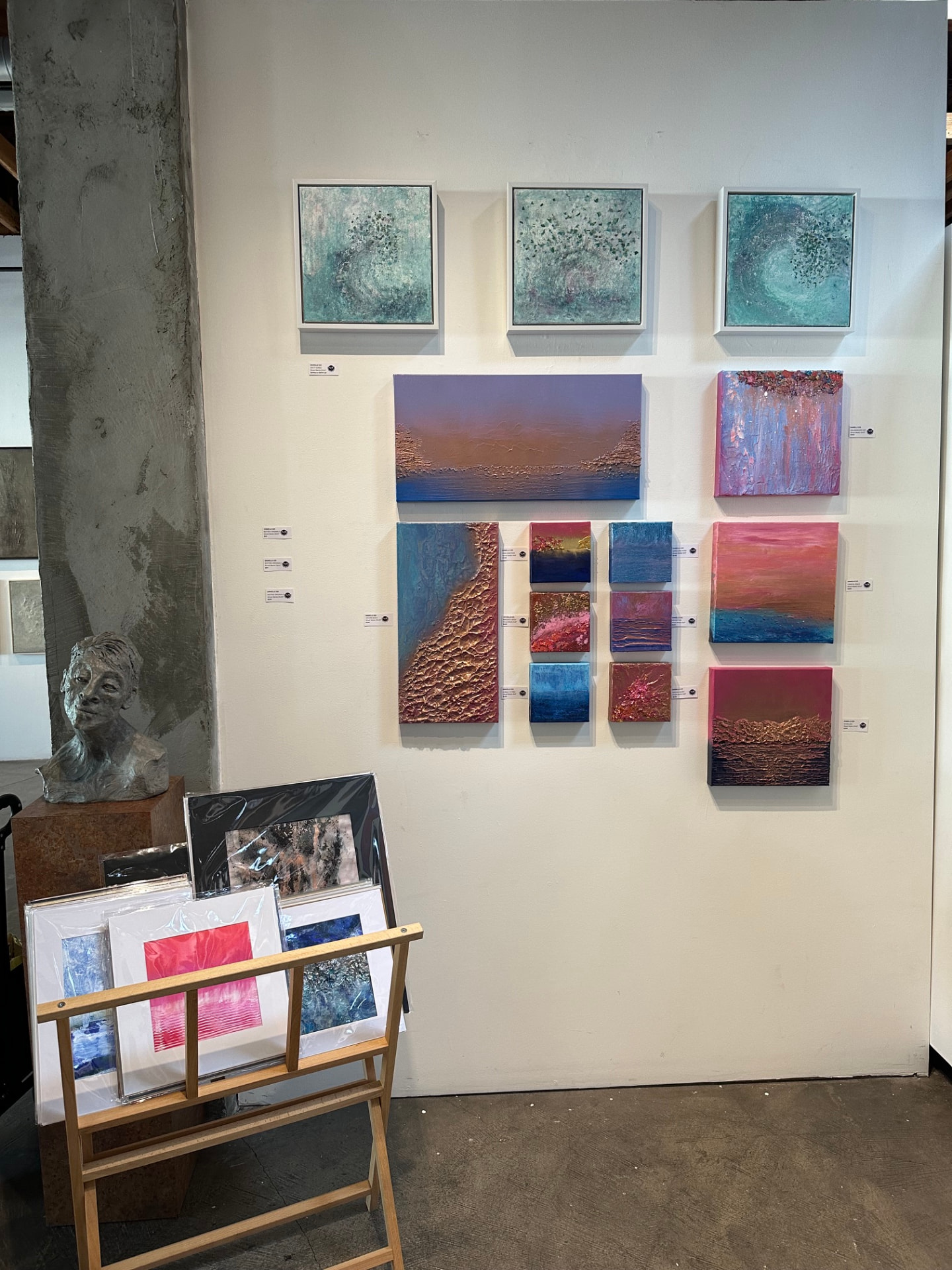 Gallery wall of small square mixed-media paintings in teal, copper, and rose